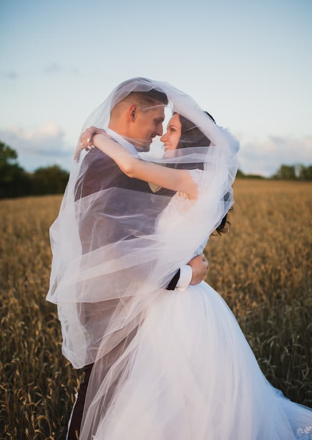 A couple embracing beneath a flowing veil outdoors